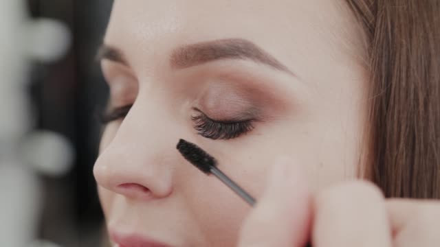 Professional-makeup-artist-woman-paints-eyelashes-to-client-of-beauty-salon