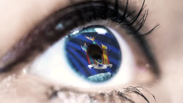 Mujer-ojo-azul-en-primer-plano-con-la-bandera-del-estado-de-Nueva-York-en-iris,-estados-unidos-de-América-con-movimiento-de-viento.-concepto-de-vídeo