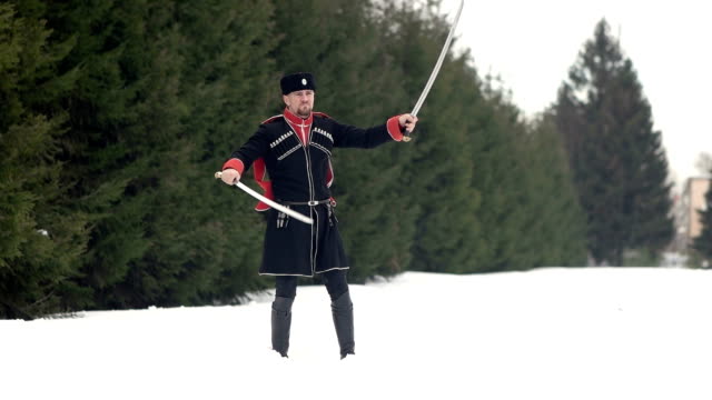 Ein-junger-Mann-in-Kosakenkleidung-schwingt-ein-Schwert-in-einer-Winterlandschaft-im-Schnee.