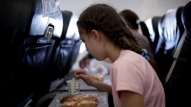 Young-woman-sits-in-chair-near-illuminator-of-airplane-and-eats-meal-for-passenger