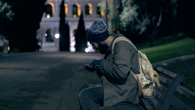homeless-man-sitting-on-a-bench-counts-money-at-night