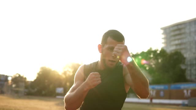 Accelerated-footage-of-an-active,-angry-male-boxer-while-training-process-on-the-outdoors-stadium.-Portrait-of-a-man-boxing-with-invisible-opponent,-punching