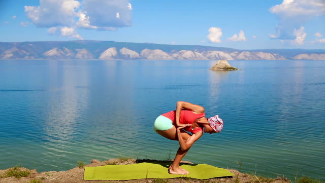 Young-professional-yoga-woman-practices-yoga-moves-outdoors-near-the-giant-blue-lake-Baikal.