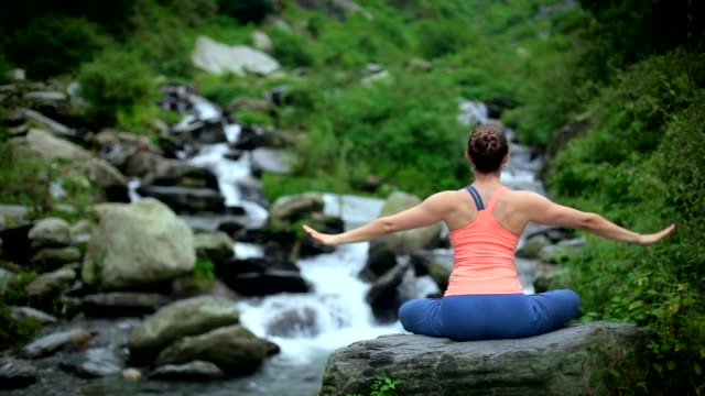 Woman-meditating-at-tropical-waterfall