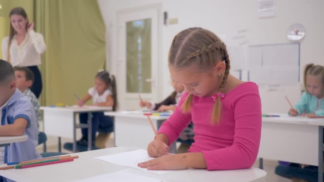 Schulmädchen-zeichnet-mit-Bleistift-auf-Papier-und-dann-schaut-die-Kamera-mit-einem-Lächeln-zeichnen-Lektion-in-einem-hellen-Klassenzimmer