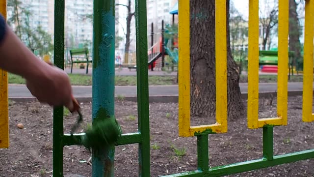 Ein-Arbeiter-grüne-Farbroller-Malerei-einen-gelb-grünen-Zaun-auf-dem-Hintergrund-Spielplatz