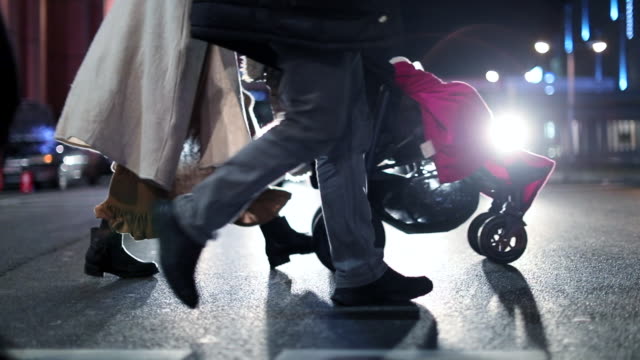 Pedestrians-crossing-street-at-night-at-120fps-slow-motion.-Lens-flares-of-cars-in-the-background-with-crowd-of-people-in-the-foreground.-Couple-with-stroller-crossing-the-street