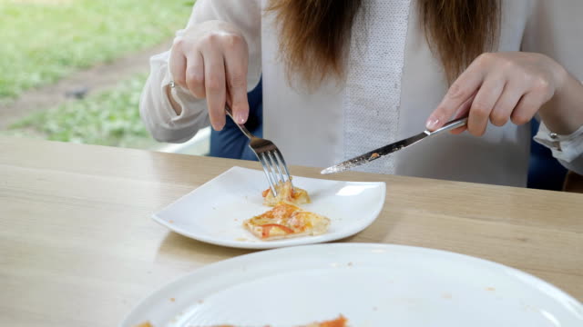 Cutting-a-piece-of-pizza-with-a-knife-and-fork-on-a-white-plate