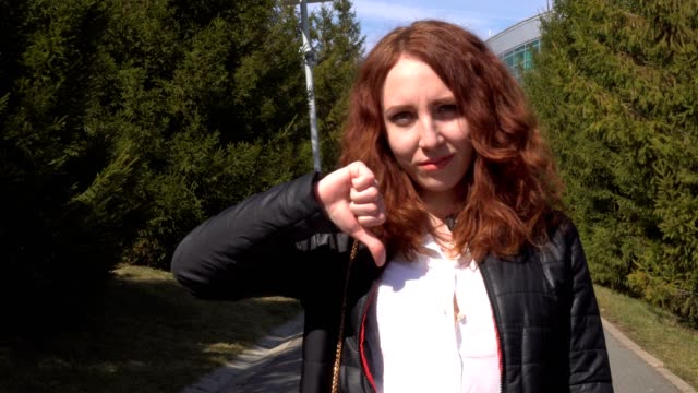 Young-beautiful-redhead-girl-student-outdoors-at-street-walking-in-park-and-showing-thumbs-down