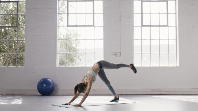 Woman-doing-one-legged-down-dog-pose-in-yoga-studio