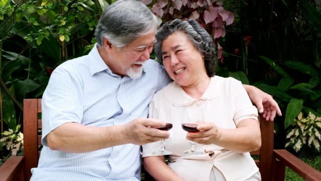 Senior-couple-sitting-and-drinking-red-wine-together-in-home-garden.