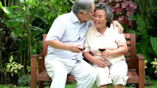 Senior-couple-sitting-and-drinking-red-wine-together-in-home-garden.