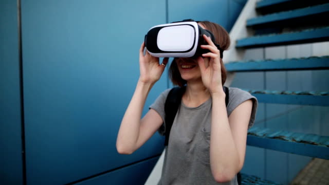 Future-is-now.-Beautiful-young-female-on-a-stairs-playing-game-in-vr-glasses.-Young-caucasian-woman-touch-something-using-modern-virtual-reality-glasses-on-a-blue-background.