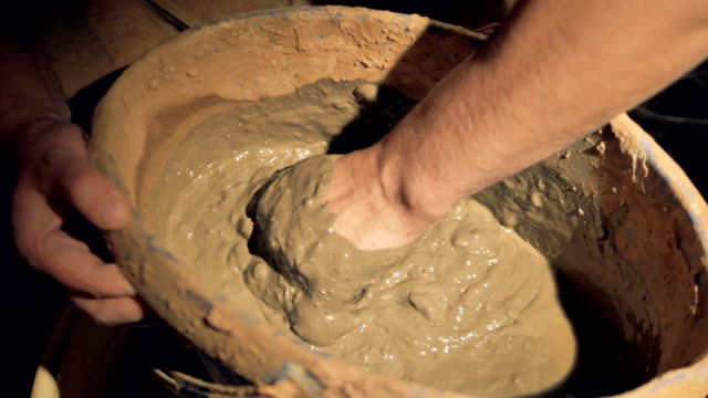 Potter-mixes-clay-by-hand-in-a-pail.