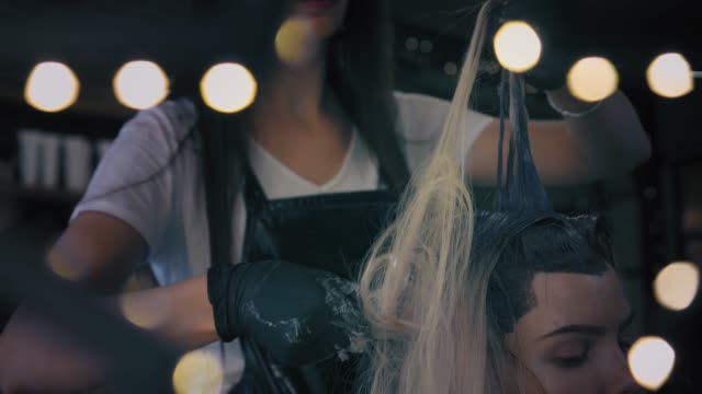 Friseur-in-professionelle-Handschuhe-teilt-lange-Frau-gefärbtes-Haar-in-Strähnen-mit-Pinsel-und-Haarfärbemittel-gilt