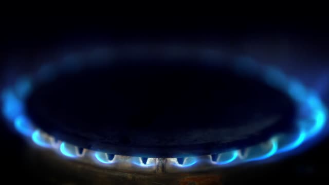 Close-up-of-gas-stove-blue-flame-lit-in-a-dark-kitchen