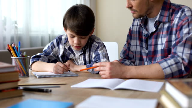 Fürsorglicher-Vater-helfen,-seinen-kleinen-Sohn-zu-tun,-Hausaufgaben,-Väter-Unterstützung,-Bildung