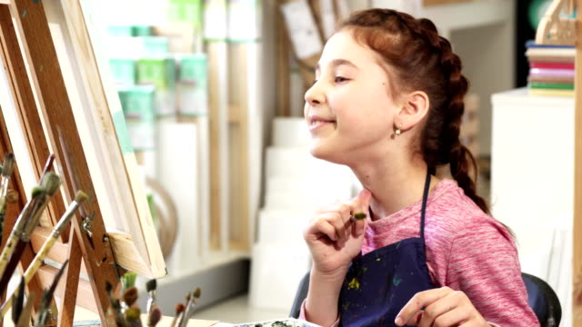 Cute-little-girl-showing-thumbs-up-while-painting-a-picture-at-the-art-class