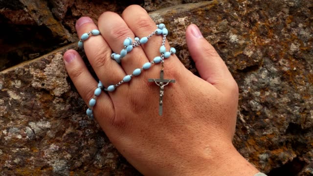Hand-with-rosary-on-stone-wall
