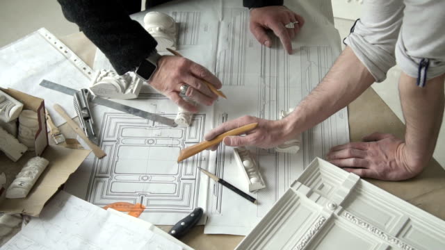 Hands-of-two-male-designers-working-on-molding-blueprint