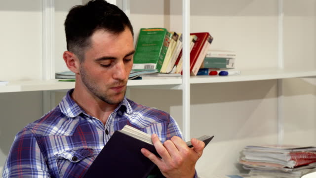 Handsome-young-man-smiling-joyfully-while-reading-a-book