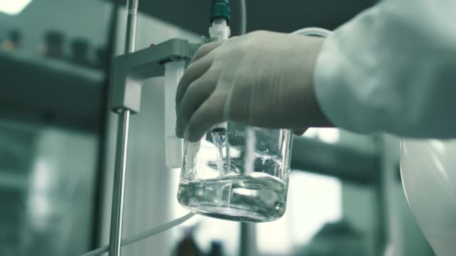 Mitarbeiter-eines-chemischen-Labors-sammelt-die-Flüssigkeit-in-eine-Tasse