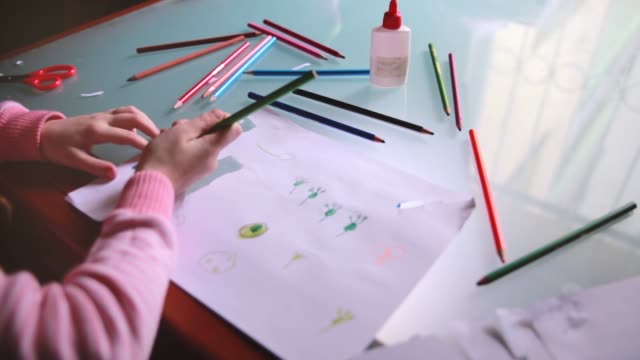 Draufsicht-Kamera-gleiten-auf-Kaukasische-Mädchen-Kind-Zeichnung-auf-Papier-mit-verschiedenen-Farbstiften-an-einem-Tisch-Links