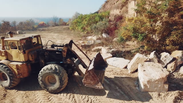 professional-bulldozer-with-a-bucket-is-picking-up-stones-on-sandy-quarry-against-the-backdrop-of-wild-nature.