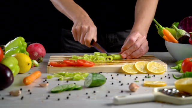 Man-is-cutting-vegetables-in-the-kitchen,-slicing-green-bell-pepper-in-slow-motion