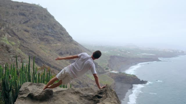 Ein-Mann-steht-auf-der-einen-Seite-in-den-Bergen-mit-dem-Rücken-zur-Kamera-mit-Blick-auf-den-Ozean-und-meditieren-auf-den-Kanarischen-Inseln.