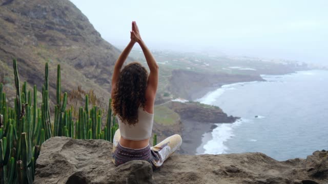 Junge-Frau-beim-Yoga-in-den-Bergen-auf-einer-Insel-mit-Blick-aufs-Meer-auf-einem-Felsen-auf-einem-Berg-meditieren-im-Lotussitz-sitzen