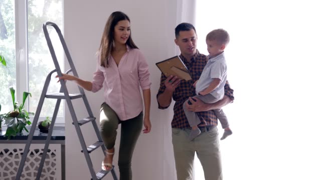 renovation-teamwork-of-flat,-happy-family-with-child-doing-repairs-in-apartment-and-hang-painting-using-stepladder-at-home