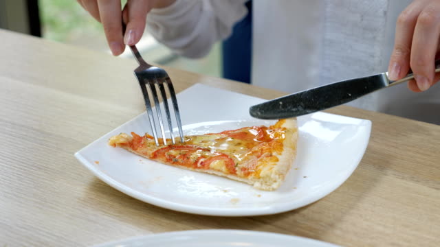 Schneiden-ein-Stück-Pizza-mit-Messer-und-Gabel-auf-einem-weißen-Teller