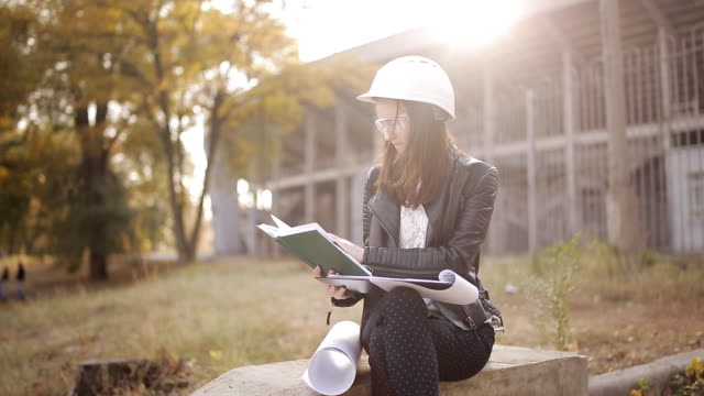 The-woman-student-architect-on-a-construction-site-examines-the-technical-documentation-and-makes-notes-in-his-notebook