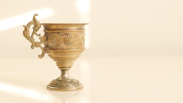 Holly-grail-look-like-ancient-object-made-of-brass-on-white-reflective-surface-4K