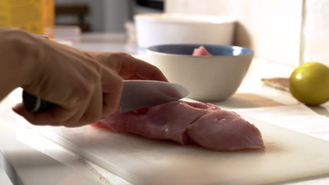 Close-up-woman-cuts-chicken-with-a-knife-on-a-Board.-Female-hands-chef-cutting-raw-chicken-meat-breast.