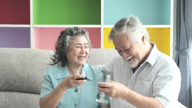 Senior-couple-sitting-and-drinking-red-wine-together-in-living-room.