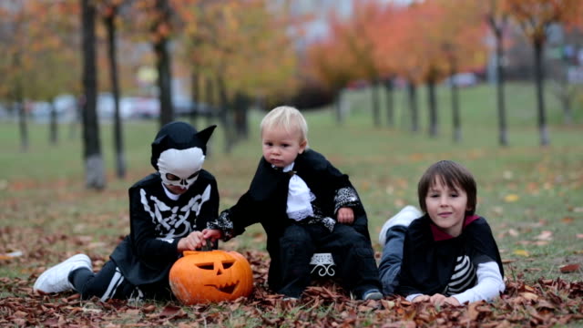 Children-having-fun-with-halloween-carved-pumpkin-in-a-park,-wearing-scary-costumes-and-playing-with-toys