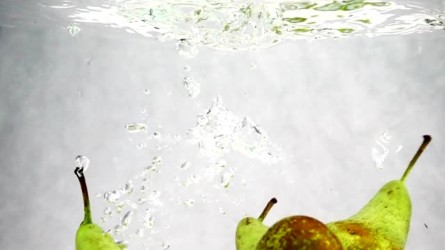 Peras-verdes-cae-al-agua-con-un-montón-de-pequeñas-burbujas.-Video-de-frutas-sobre-fondo-blanco-aislado.