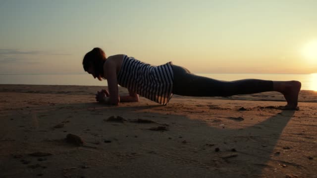 Active-young-woman-streching-and-practicing-yoga-on-beach-at-sunset.