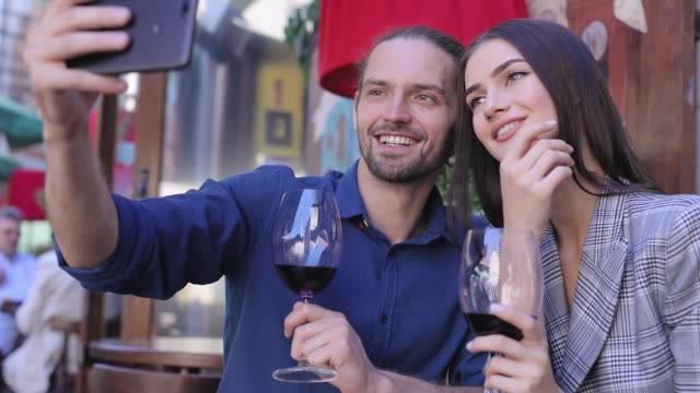 Happy-Couple-With-Wine-Taking-Photos-On-Phone-At-Restaurant
