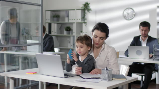 Businesswoman-Working-at-Desk-with-Child-on-Knees