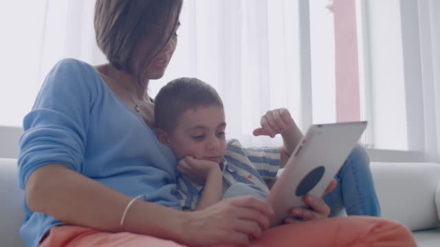 Mutter-und-Sohn-spielen-mit-digitalen-Tablet-zu-Hause.-Junge-Mutter-mit-ihrem-5-Jahre-alt-lächelnd-mit-digitalen-Tablet-zu-Hause.
