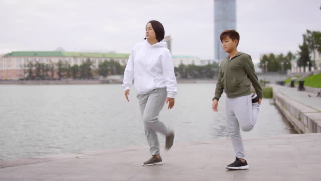 Asiatische-Mutter-und-Sohn-tun-Stretching-Übung-auf-urban-Riverside-Sidewalk