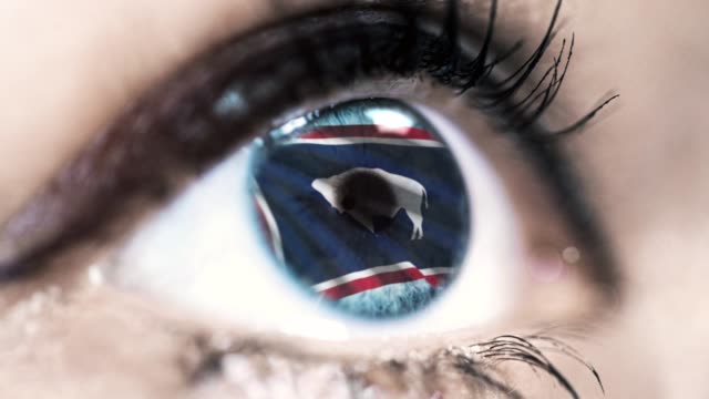 Woman-blue-eye-in-close-up-with-the-flag-of-Wyoming-state-in-iris,-united-states-of-america-with-wind-motion.-video-concept
