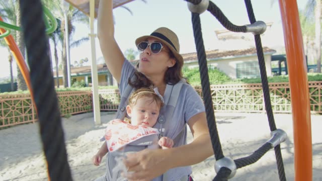 Woman-enjoying-playground-with-her-baby-in-a-carrier