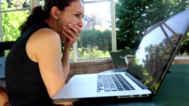 Disparo-casual-de-mujer-bostezando-frente-a-la-pantalla-de-su-computadora.-Mujer-de-30-años-trabajando-desde-su-casa-balcón.
