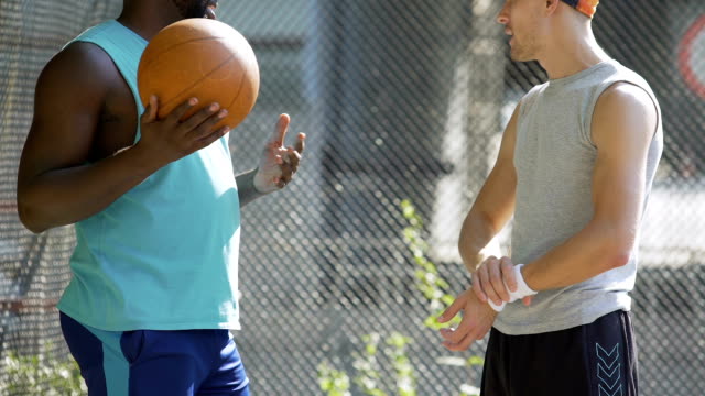 Zwei-sportliche-multirassische-Freunde-diskutieren-letzten-Basketball-Spiel-im-Stadion
