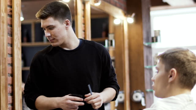 Professional-stylist-cuts-beard-of-young-man-with-electric-razor-in-barbershop