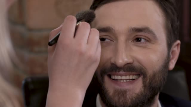 Bearded-man-actor-is-smiling-while-getting-makeup-before-filming.